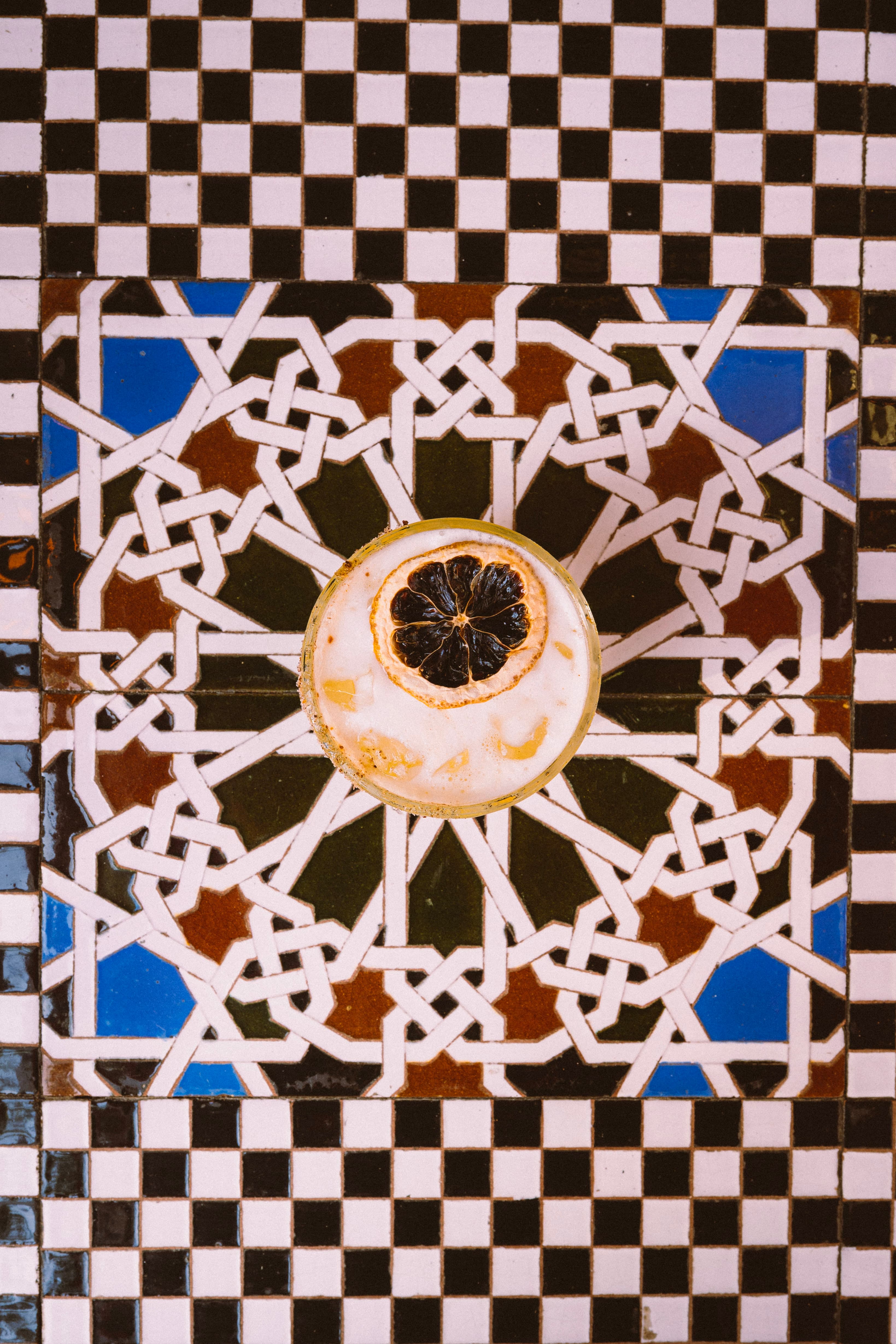A cocktail with a dried citrus garnish on a mosaic table