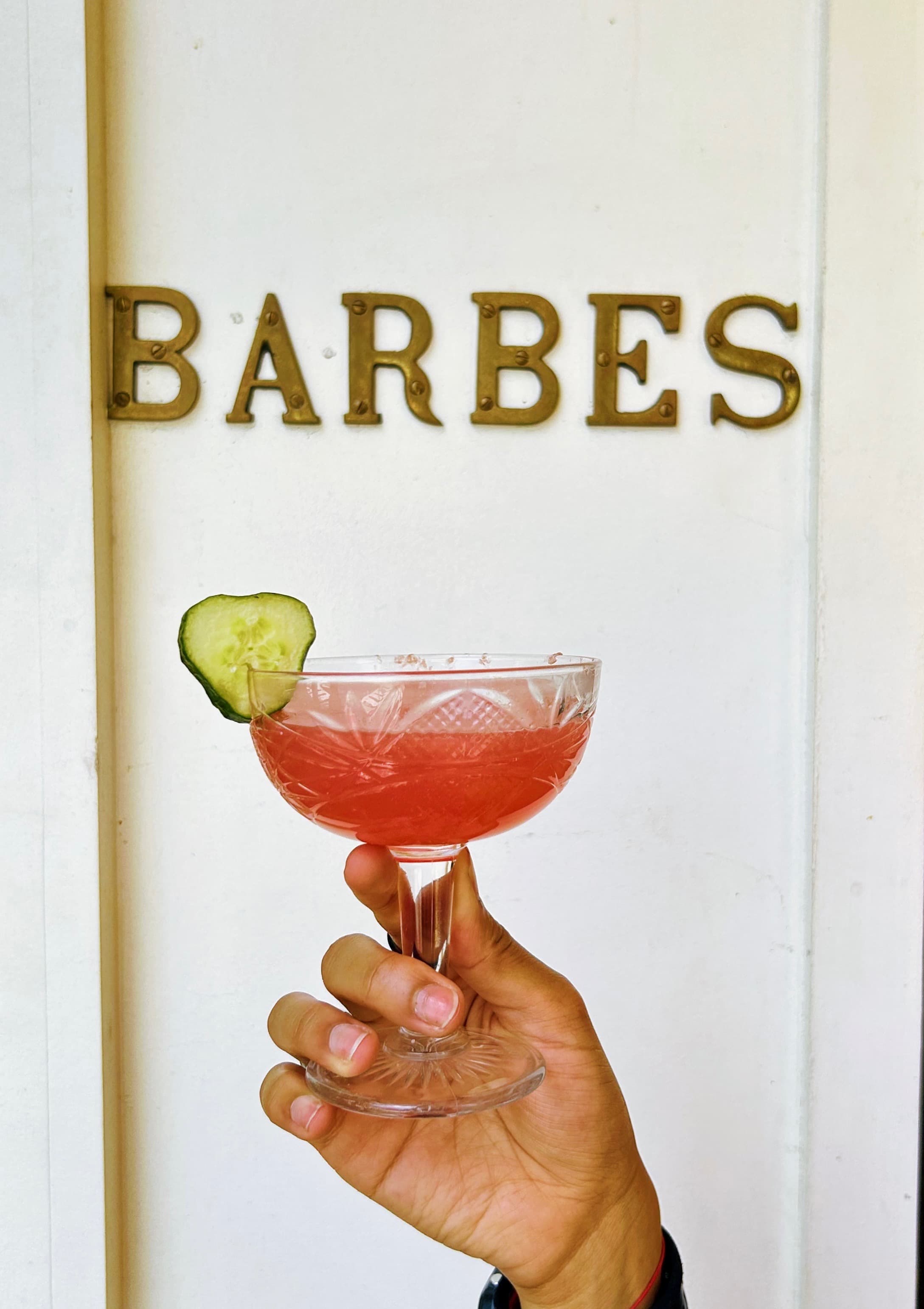 A cocktail with cucumber in front of the Barbès sign