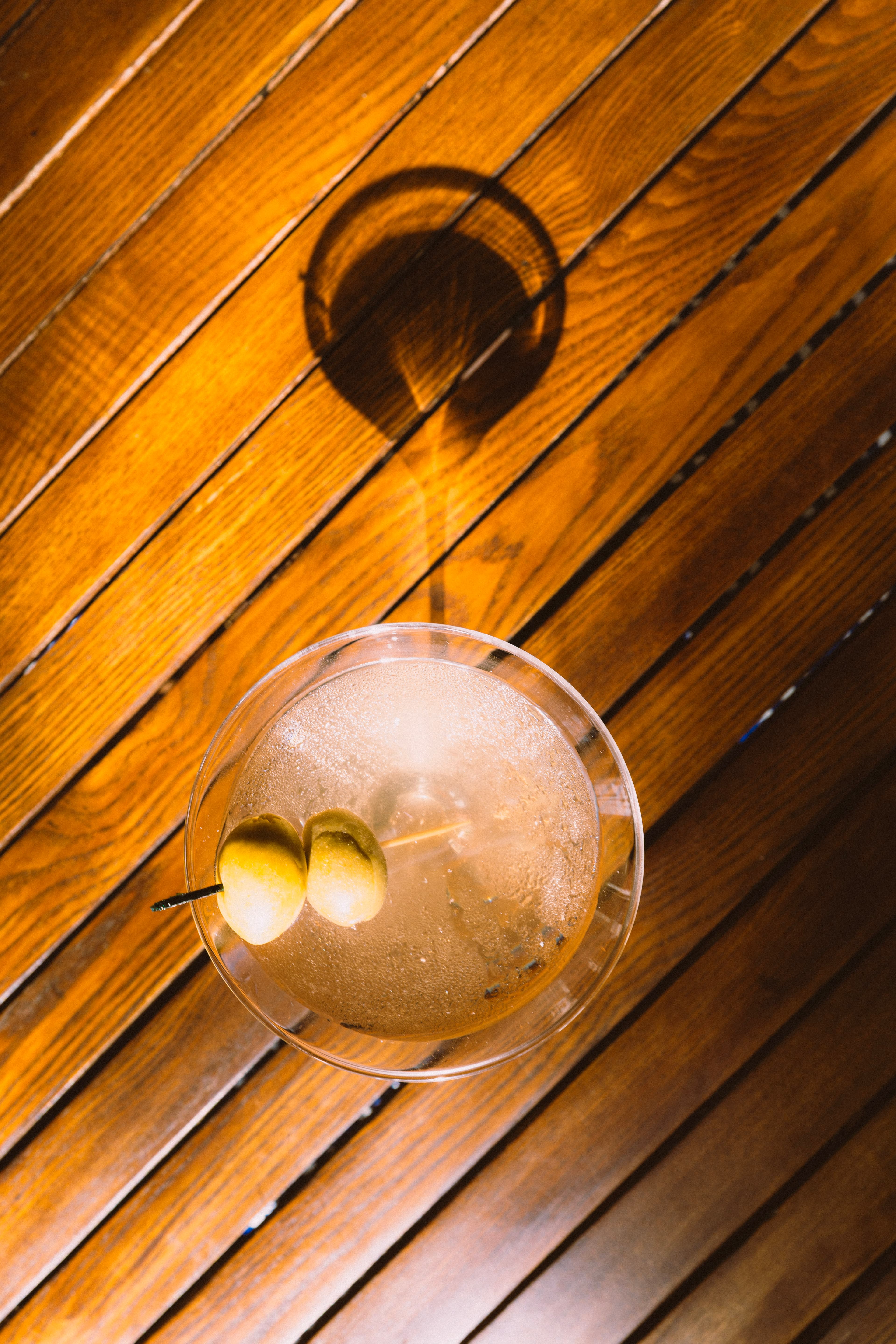 A dirty martini with olives on a wood table, seen from above