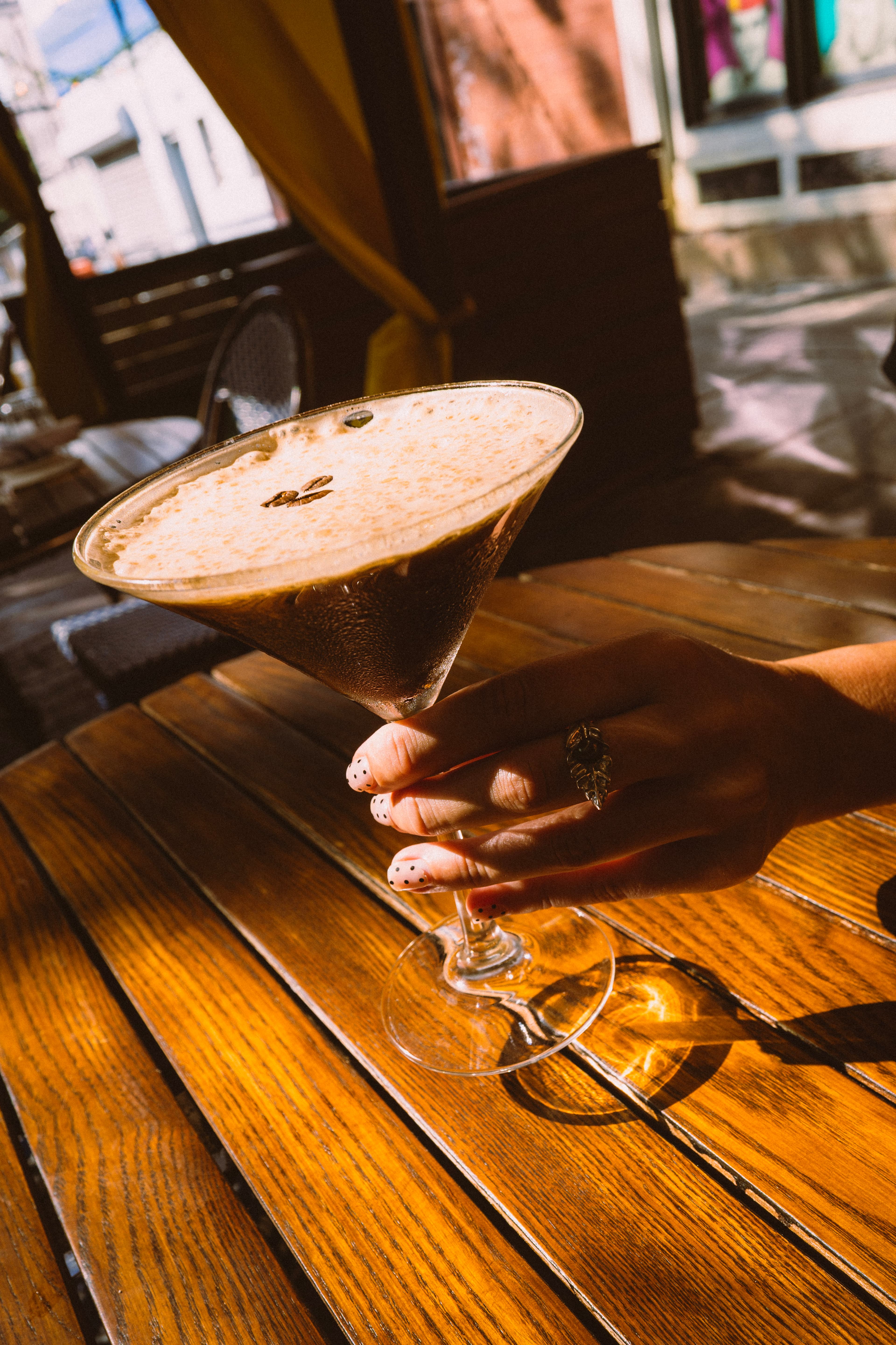 An espresso martini held over a wooden terrace table