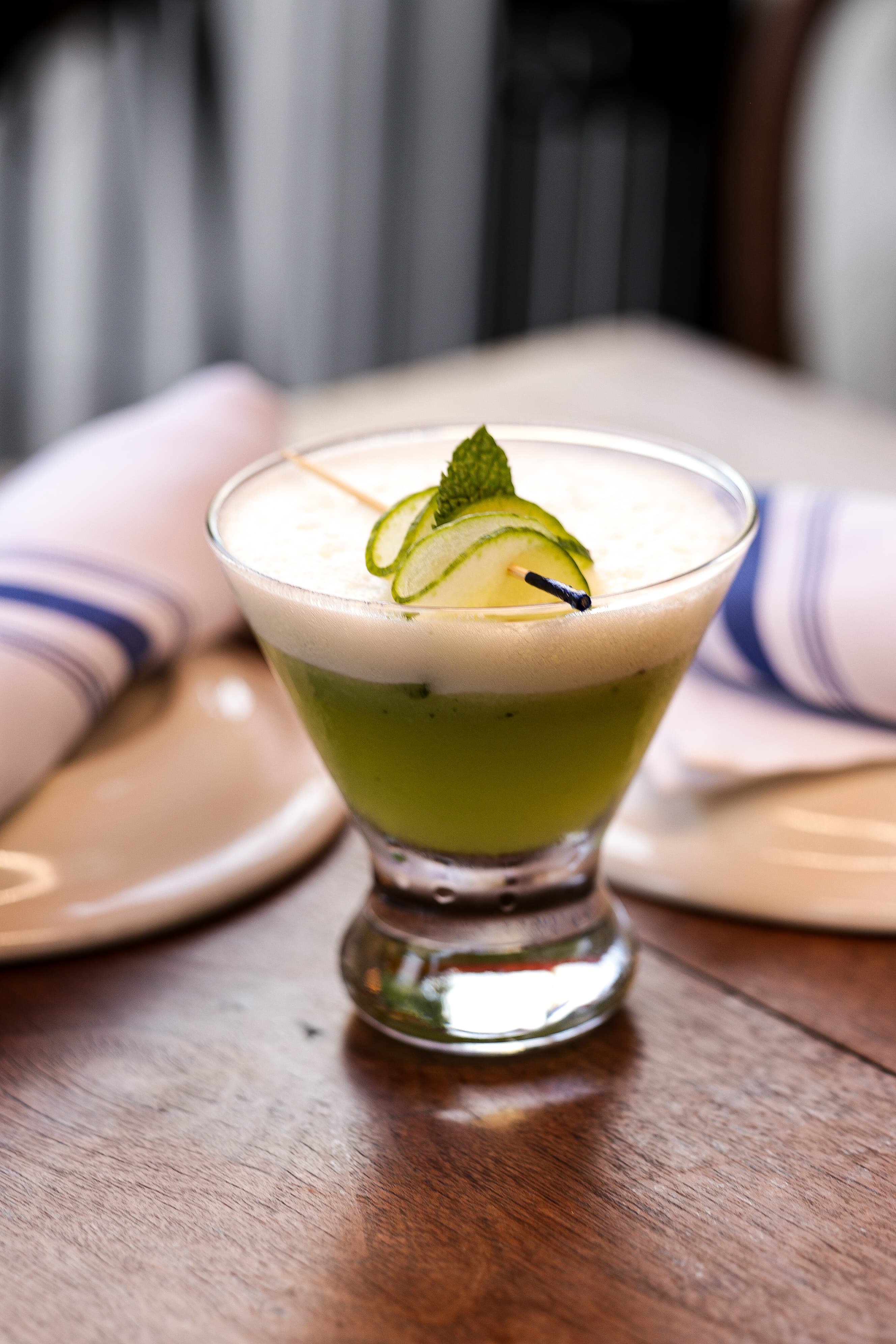A green cocktail with cucumber garnish