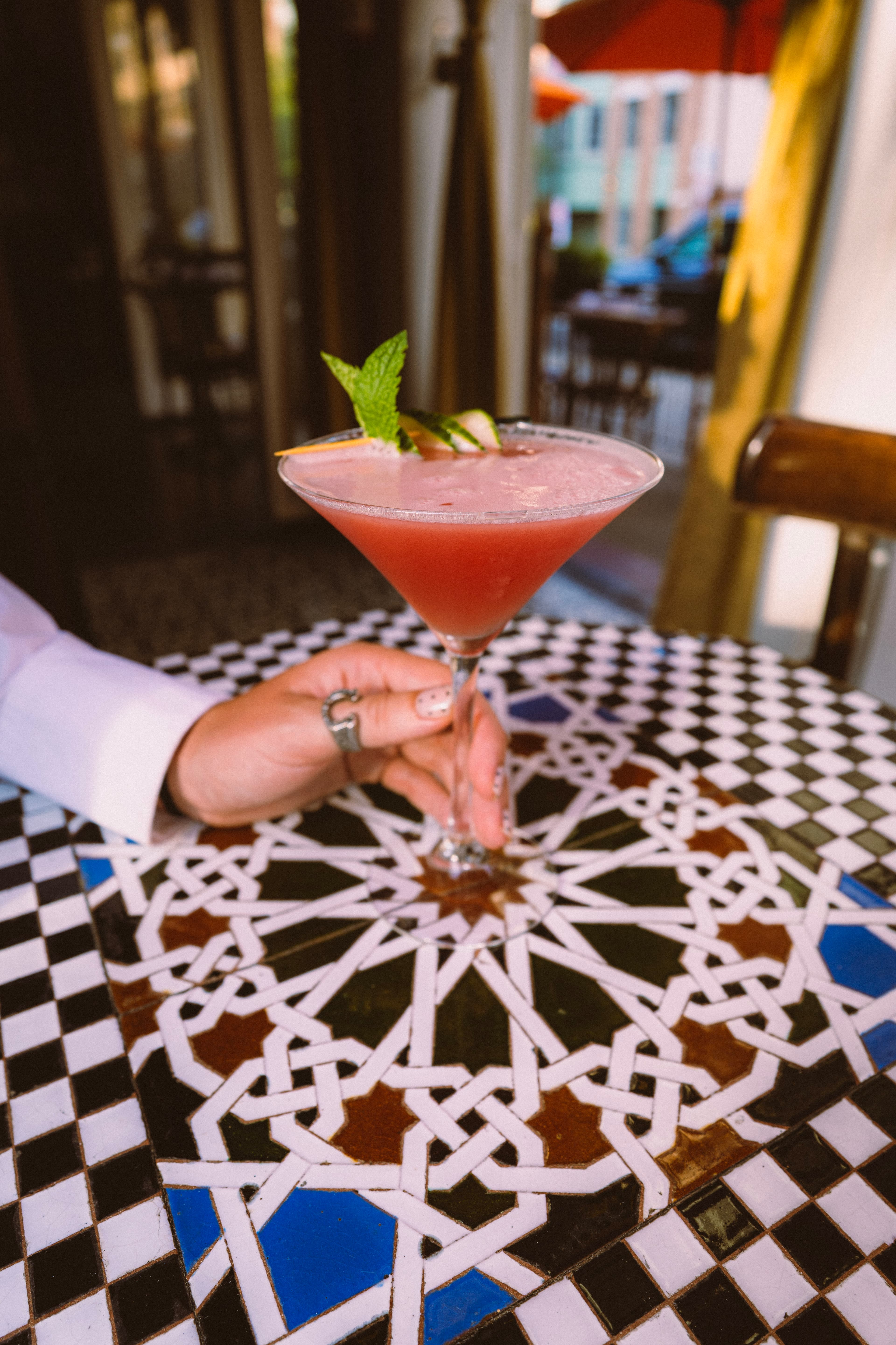 A hand holding a pink cocktail over a Moroccan tile table