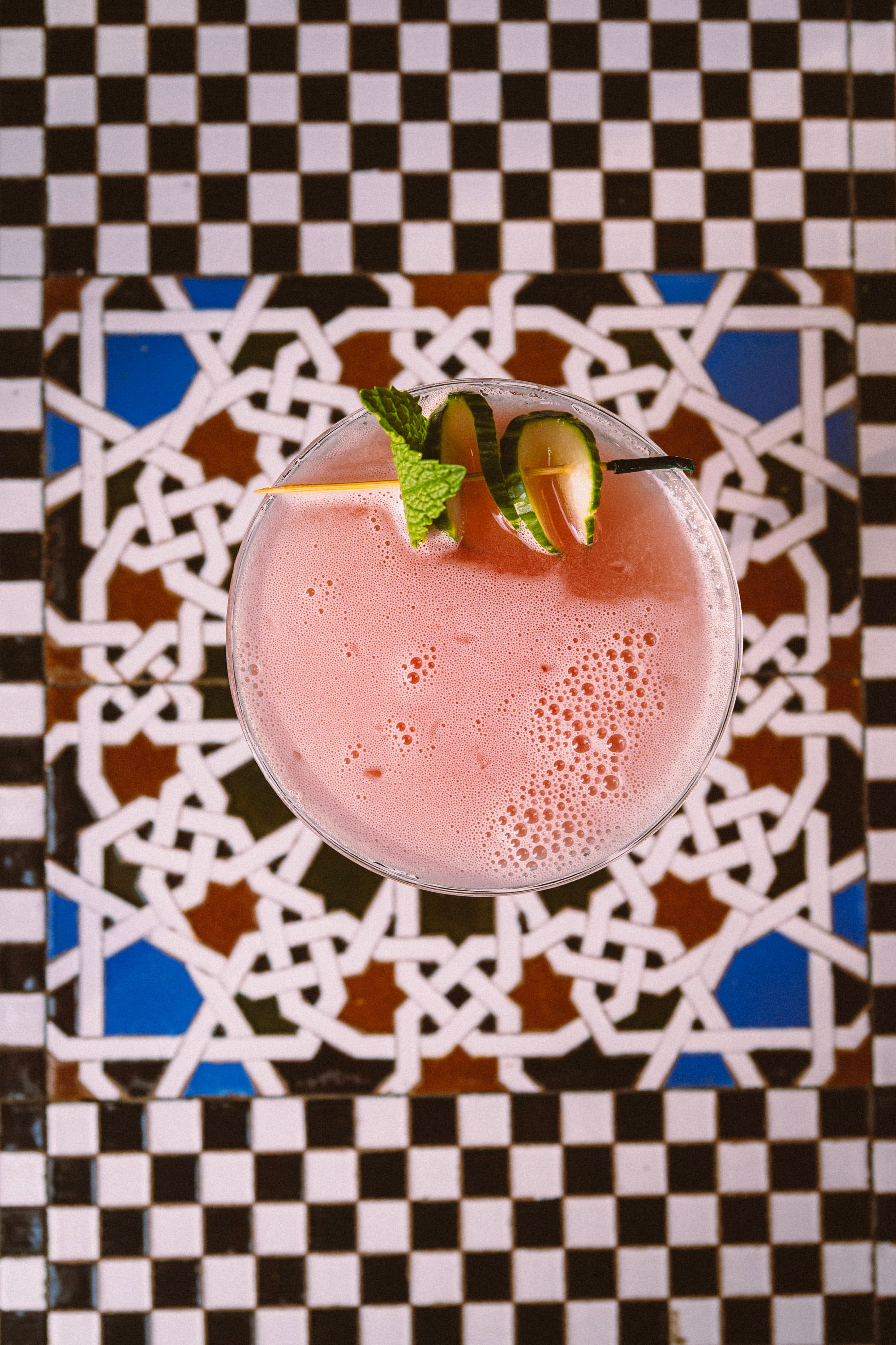 A pink cocktail with mint and lime on a mosaic table