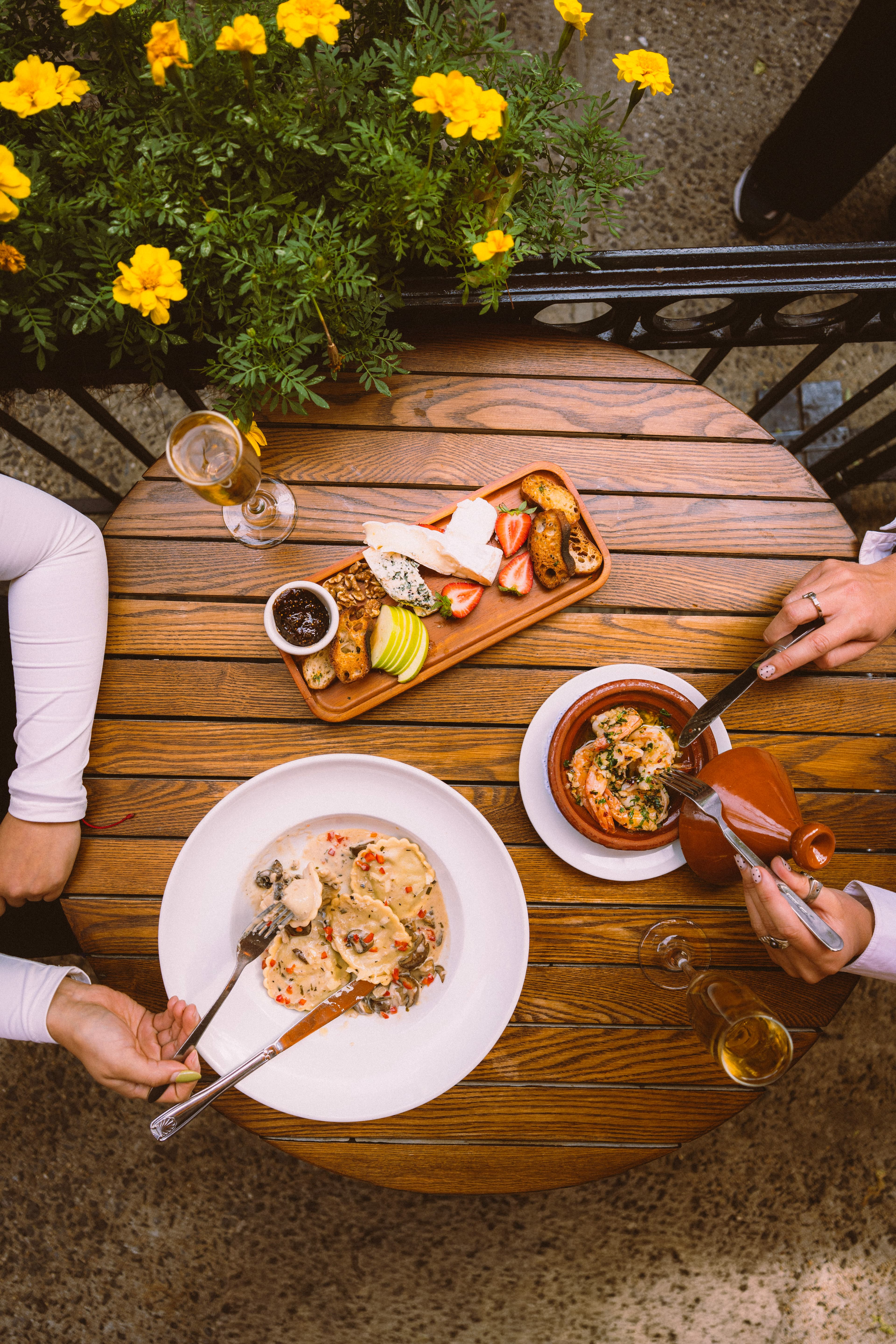 A patio table with a cheese board, ravioli and tagine, seen from above