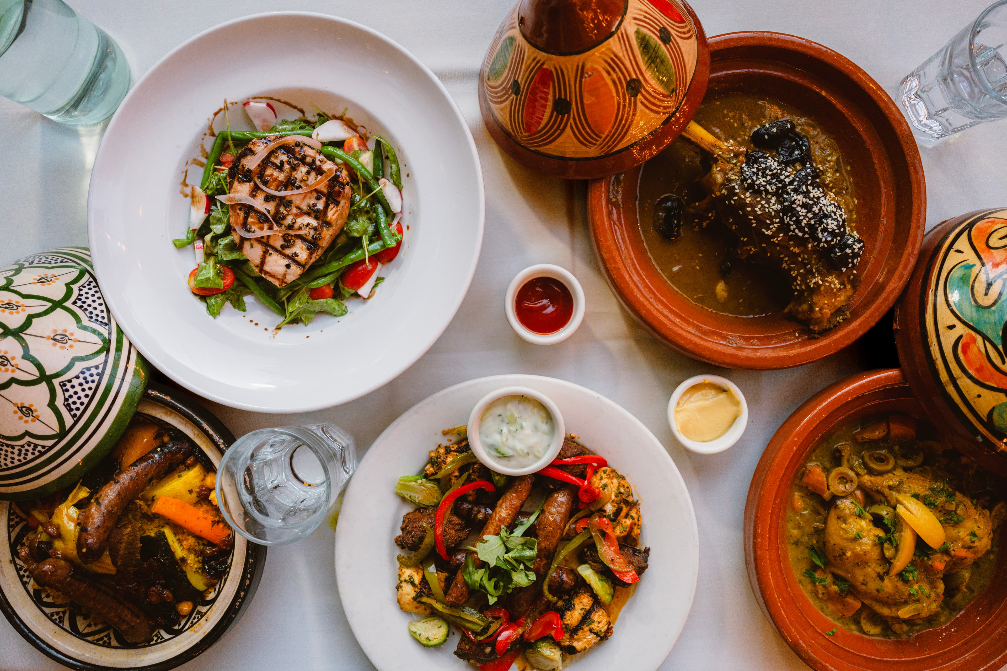 An overhead spread of tagines and salads on a white tablecloth